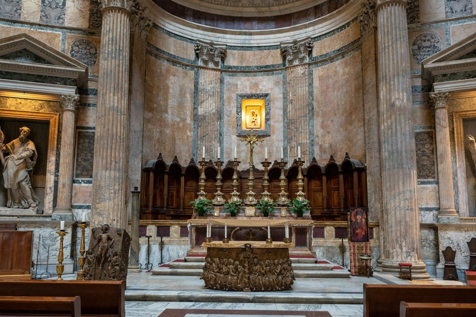 The altar inside the Pantheon in Rome, featuring ancient marble columns, an ornate altar, religious artwork, and classical Roman architecture.