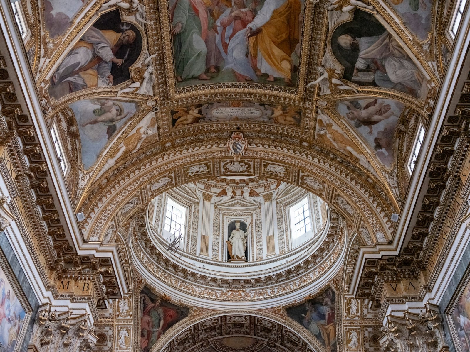 Lavishly decorated Baroque church interior in Rome with gilded arches, ornate stucco, and colorful ceiling frescoes viewed from below.