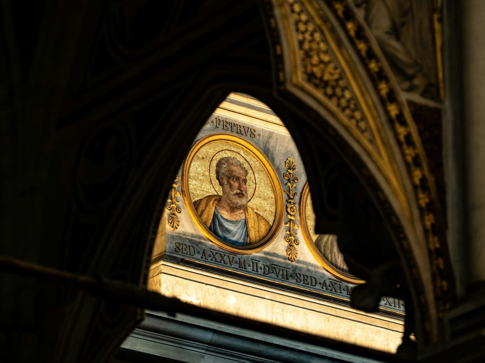 Mosaic portrait of a saint or apostle seen through a gothic church archway, illuminated inside a Roman church.