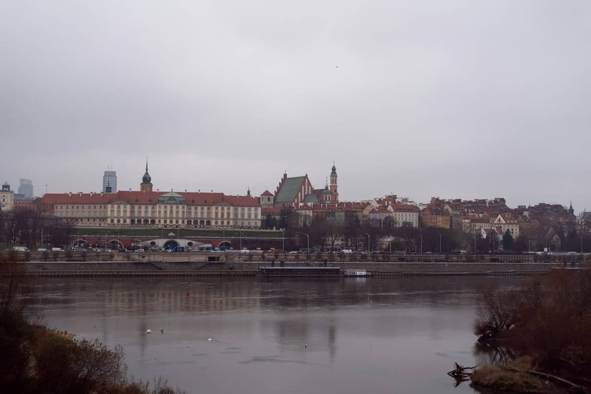 Szeroki widok na panoramę Starego Miasta w Warszawie po drugiej stronie rzeki z widocznymi czerwonymi dachami i wyraźnymi wieżami kościołów