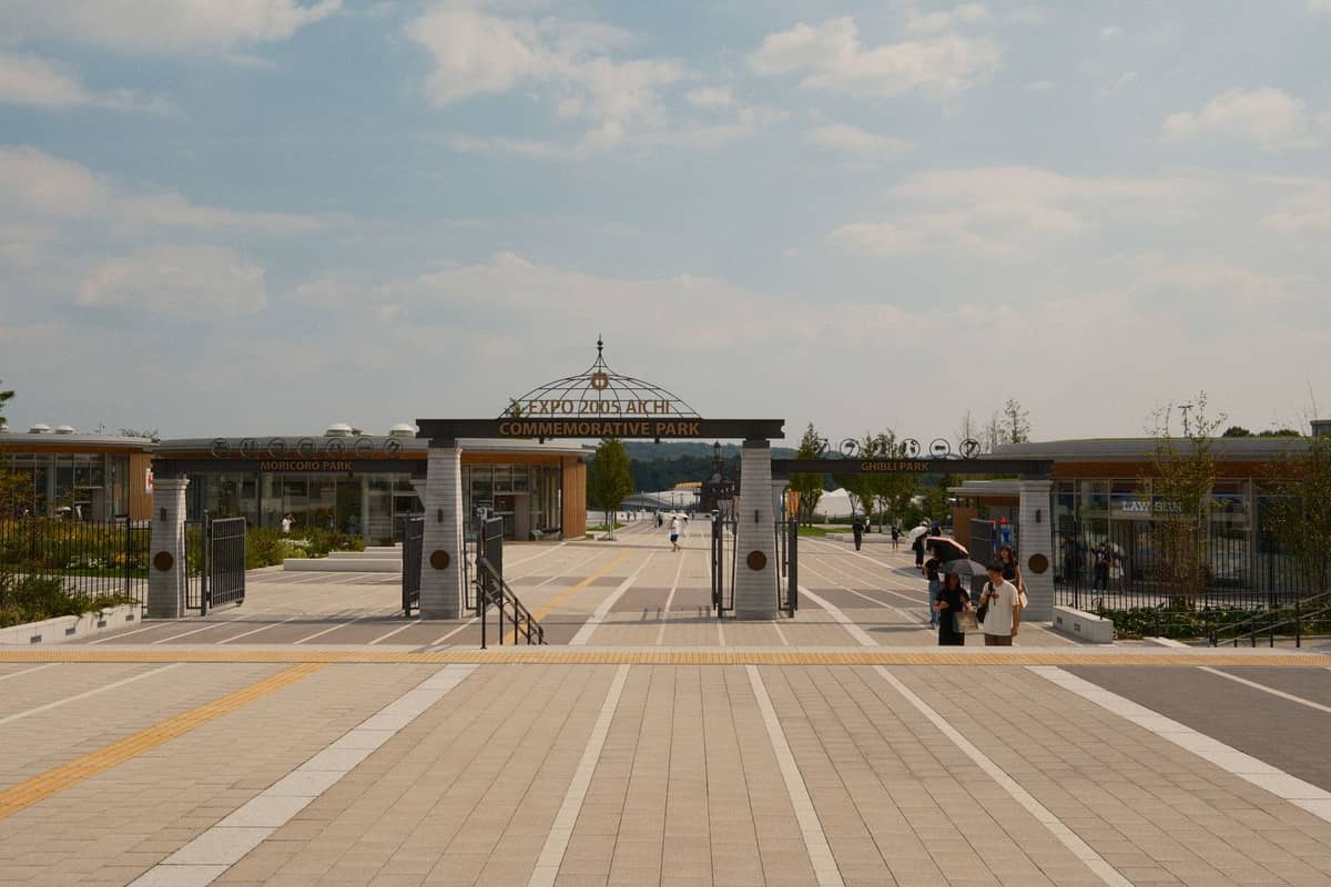 Wide entrance to Expo Commemorative Park in Osaka, with gates, pathways, greenery, and people entering on a sunny day.