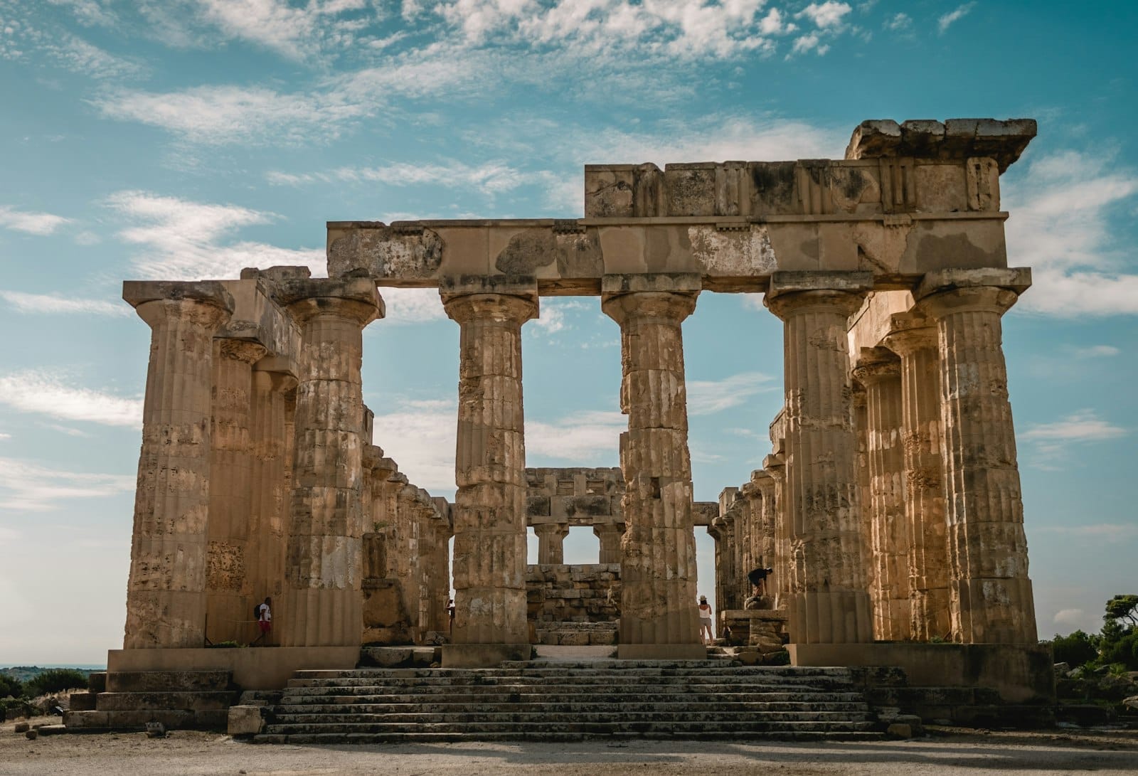 Frontansicht eines antiken griechischen Tempels in Sizilien mit hohen Steinsäulen unter einem strahlend blauen Himmel mit vereinzelten Wolken.