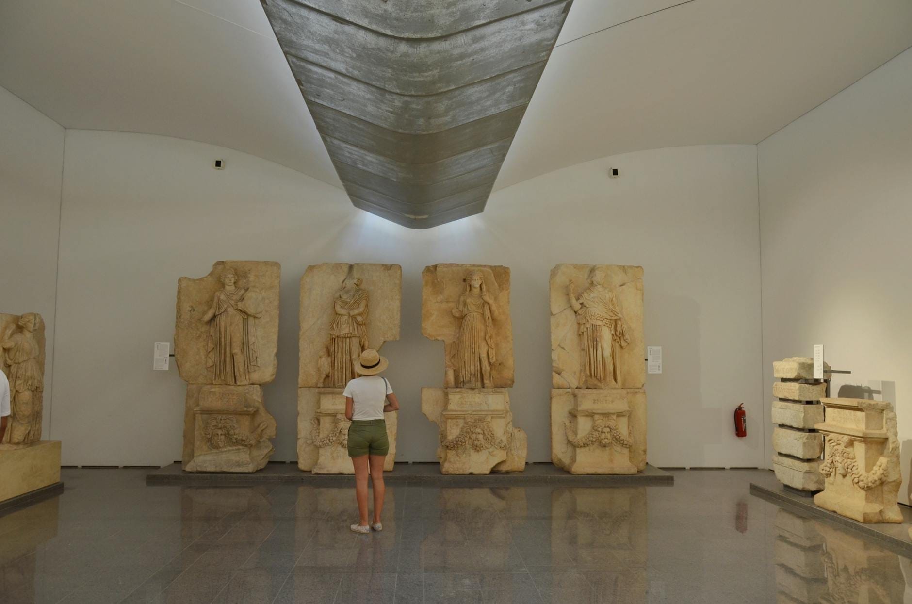 Eine Person steht in einem modernen archäologischen Museum und betrachtet große antike Steinreliefs in einer gut beleuchteten Galerie.