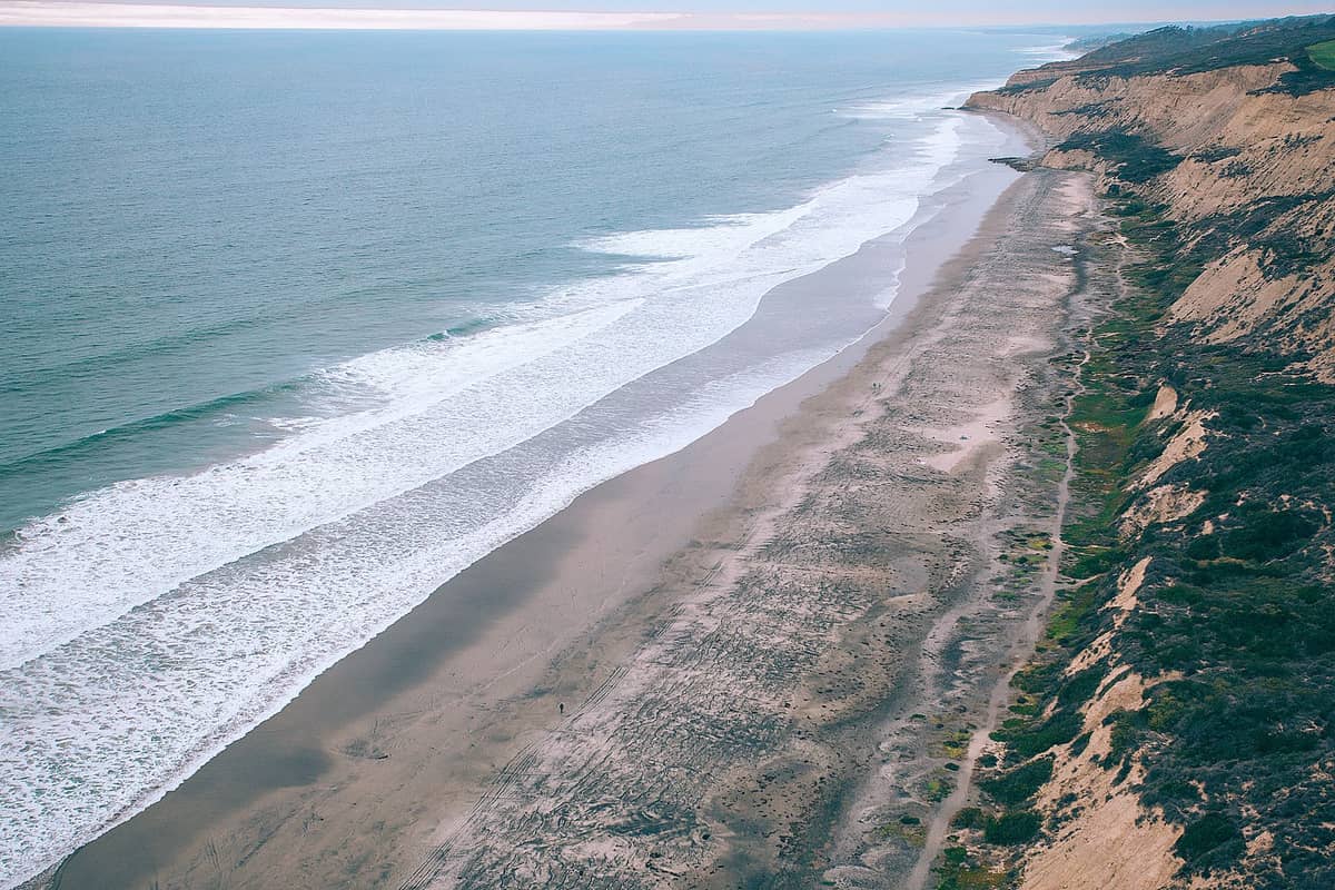 ภาพมุมสูงของหน้าผาชายฝั่งสูงชันพร้อมหาดทรายและคลื่นตามแนว Torrey Pines State Reserve ในซานดิเอโก