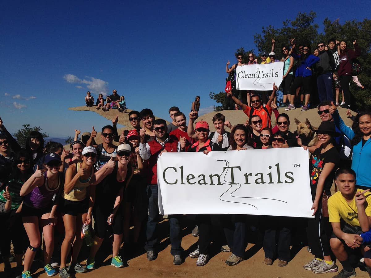 กลุ่มนักเดินป่าขนาดใหญ่ที่ Potato Chip Rock ใน San Diego ถือป้าย Clean Trails พร้อมนักเดินป่านั่งอยู่บนยอดหินที่มีชื่อเสียง