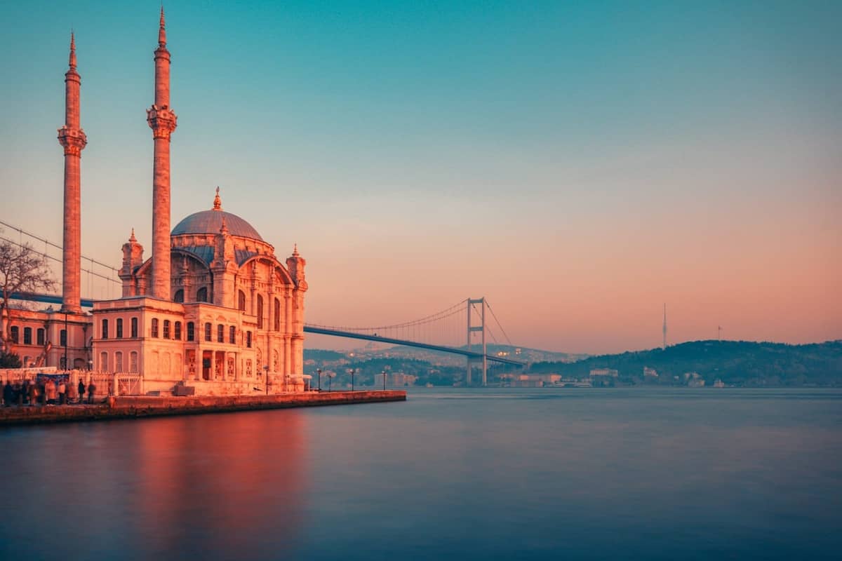 Una mezquita frente al mar con dos minaretes junto al Puente del Bósforo al atardecer en Estambul, pintoresca e invitante.