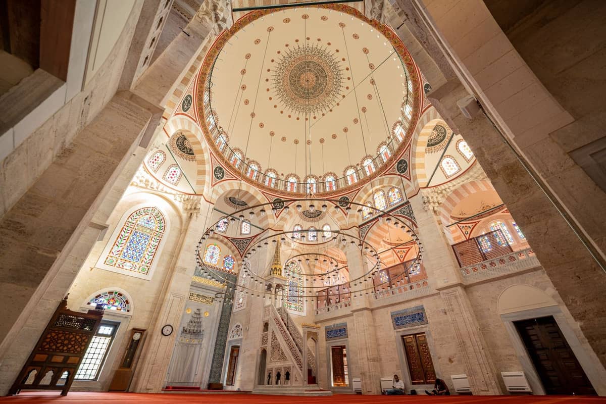 Vista gran angular del interior de una gran mezquita en Estambul con una cúpula ornamentada, vidrieras y detalles arquitectónicos intrincados.