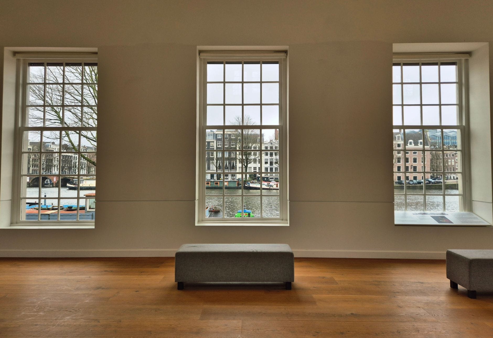 Vista interior de un tranquilo espacio de museo en Ámsterdam con grandes ventanas que dan al canal y edificios históricos.