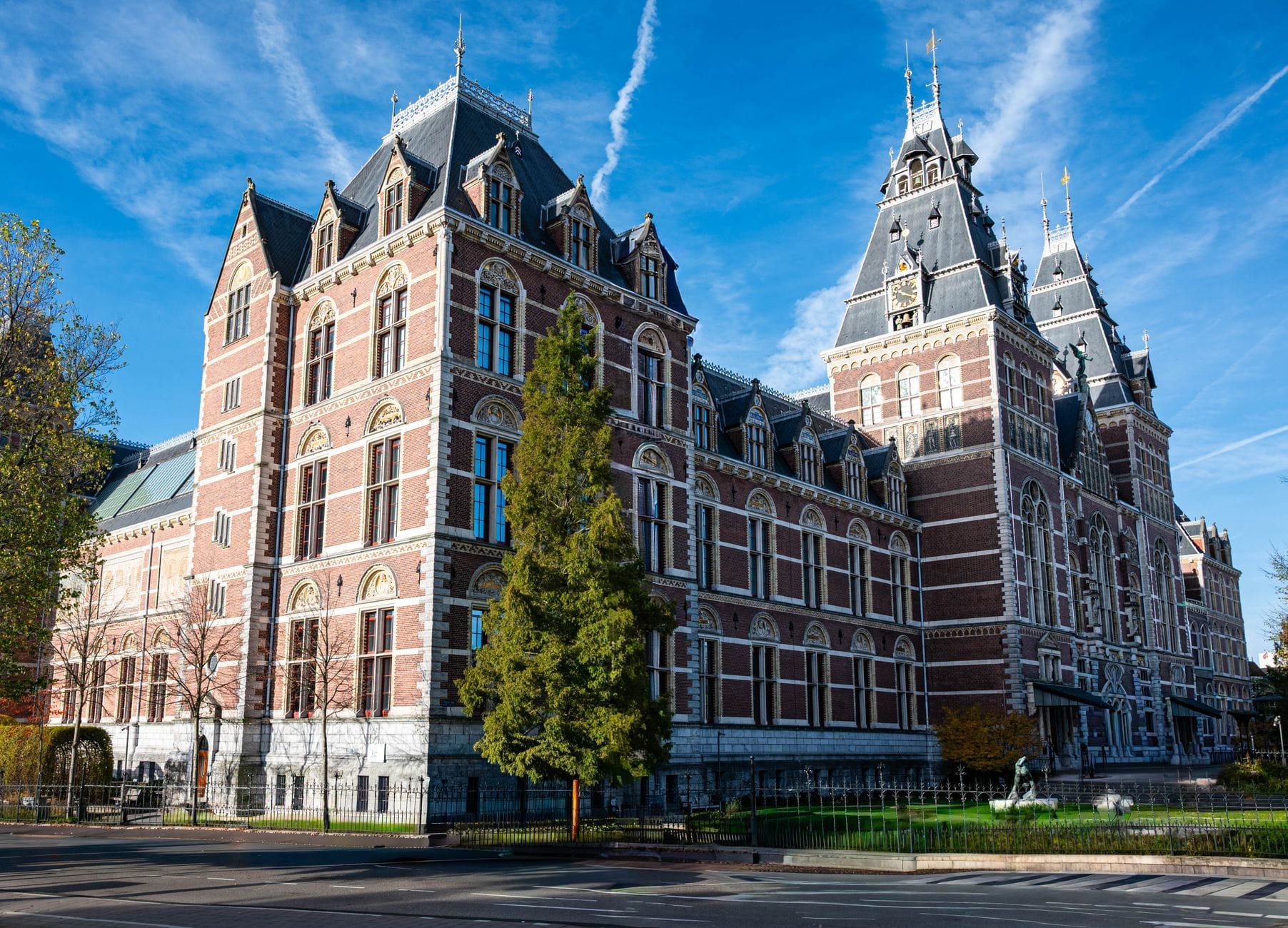 Gran edificio de museo de ladrillo rojo ornamentado con torretas y agujas bajo un cielo azul, probablemente el Rijksmuseum en Ámsterdam.