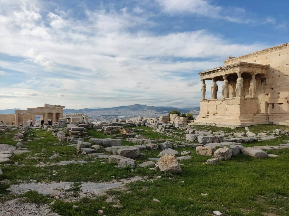 Erechtheion-Tempel mit Karyatidenfiguren und archäologischen Ruinen auf dem Akropolis-Hügel unter blauem Himmel in Athen, Griechenland.