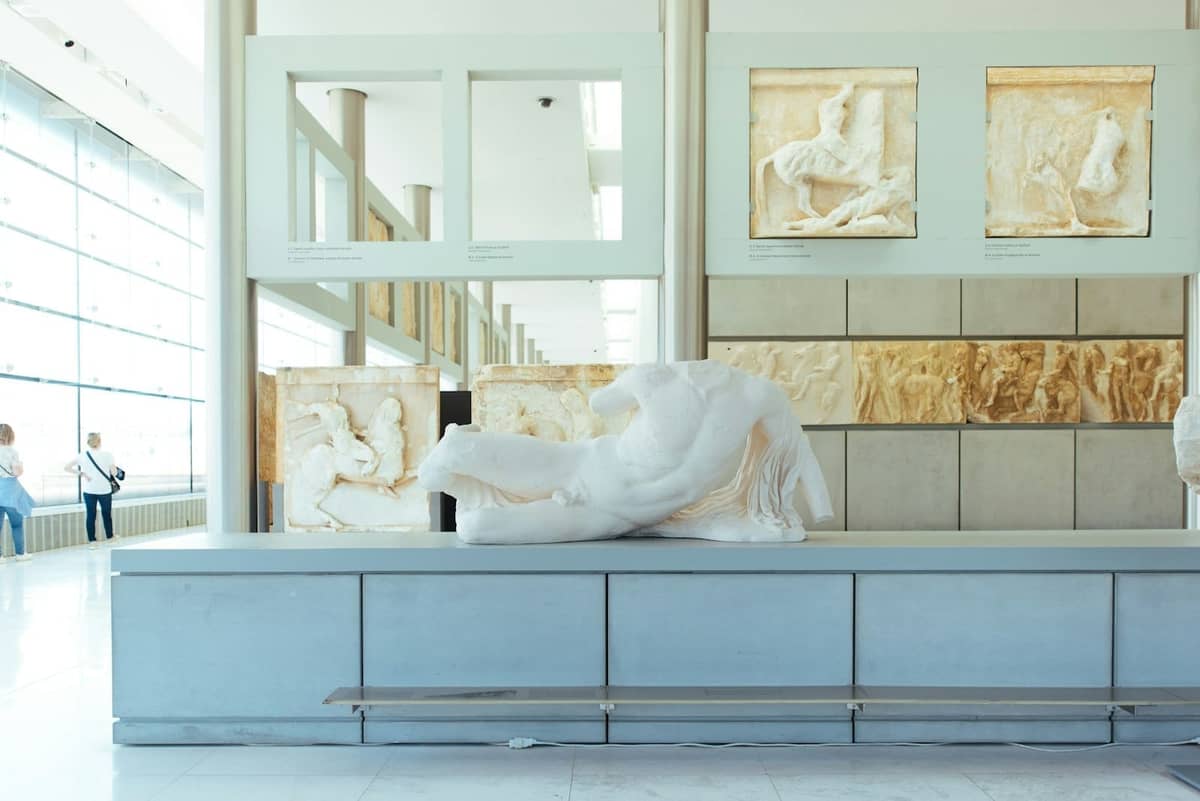 Innenraum eines hellen archäologischen Museums mit antiken griechischen Marmorskulpturen und Friesen, großen Fenstern und modernem Design.