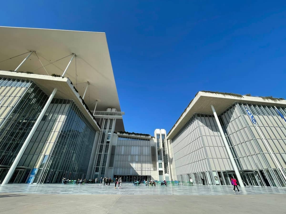 Modernes Stavros Niarchos Foundation Cultural Center in Athen mit Glasfassade, blauem Himmel und Menschen auf dem Platz davor