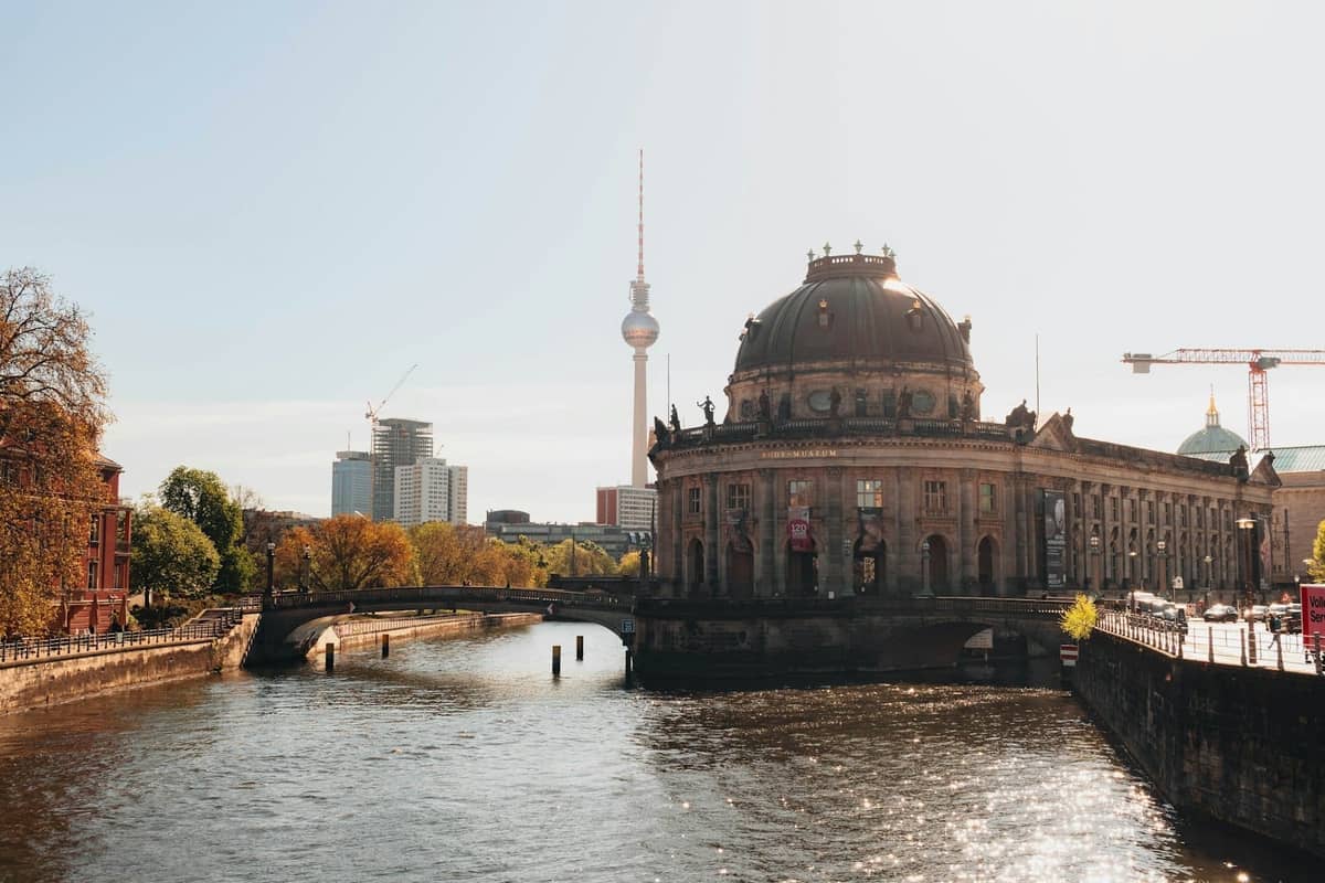 Das Bode-Museum auf der Berliner Museumsinsel, mit der Spree, Bäumen, einem Ausflugsboot und dem Berliner Fernsehturm im Hintergrund.