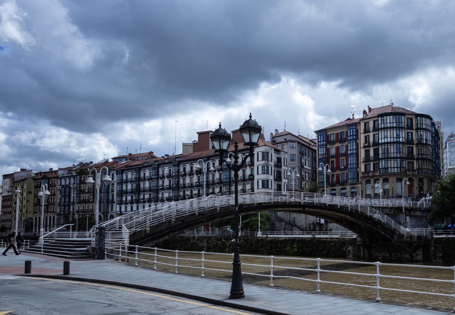 Widok na nabrzeże Bilbao z klasyczną architekturą miejską i mostem dla pieszych pod dramatycznym niebem