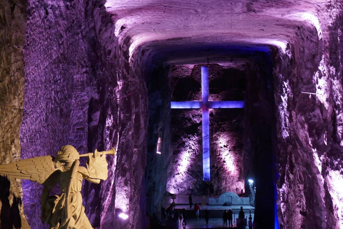 Interior of the Salt Cathedral of Zipaquirá with illuminated cross and angel sculpture, purple lighting highlighting the carved rock walls.