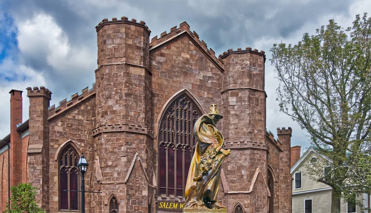 Vista exterior de un museo de estilo gótico de piedra en Salem con una estatua de una figura al frente y árboles cercanos.