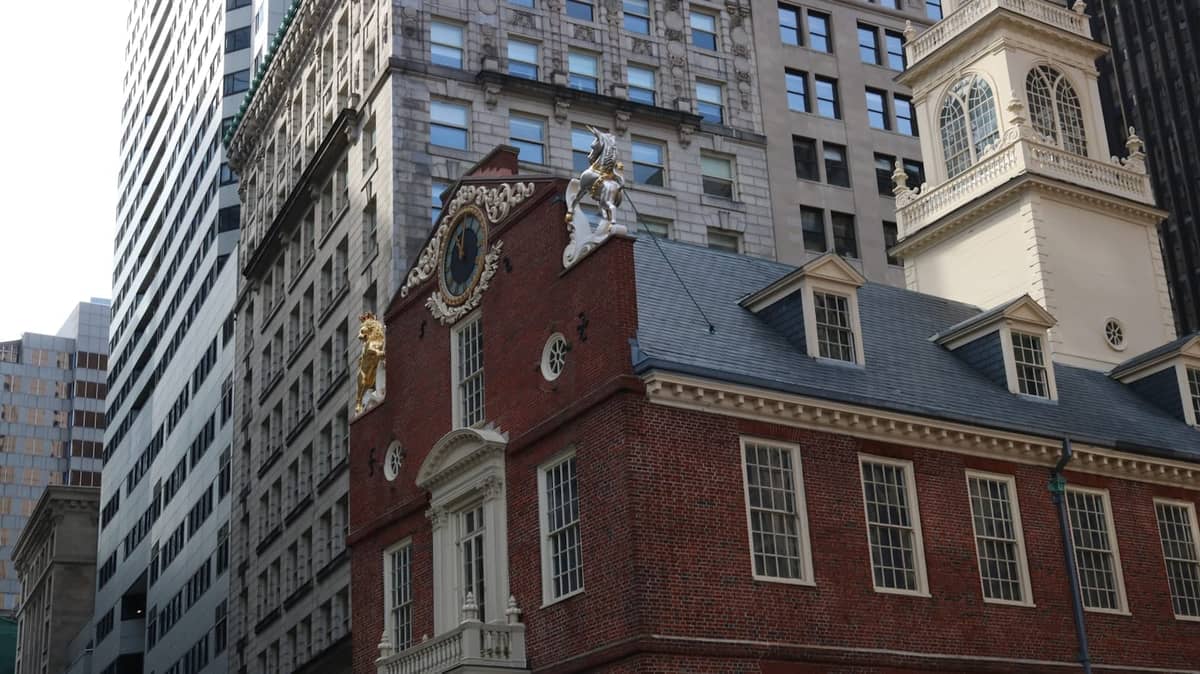 Histórico edificio de ladrillo y molduras blancas del Old State House rodeado de rascacielos modernos en el centro de Boston, visto desde el nivel de la calle.