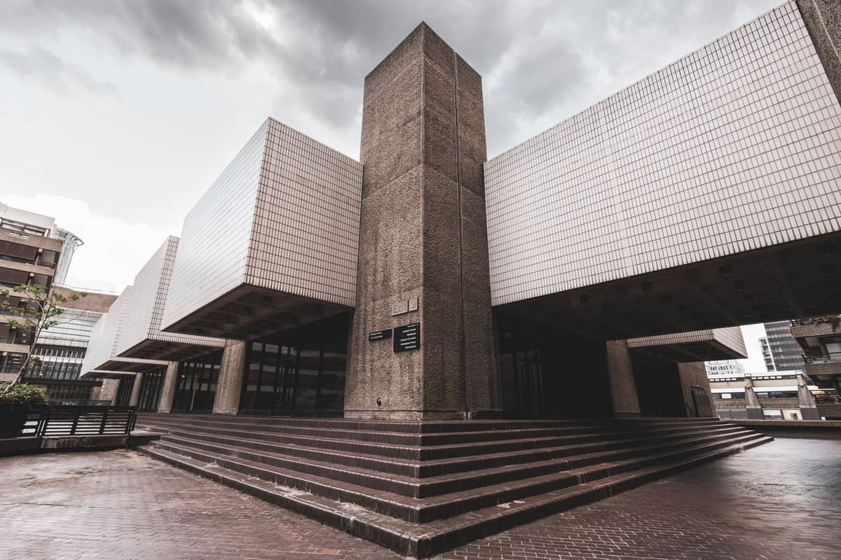 Modernong panlabas na bahagi ng isang museo ng sining na may mga geometric na hugis at teksturadong plaza sa harap, sa ilalim ng maulap na langit
