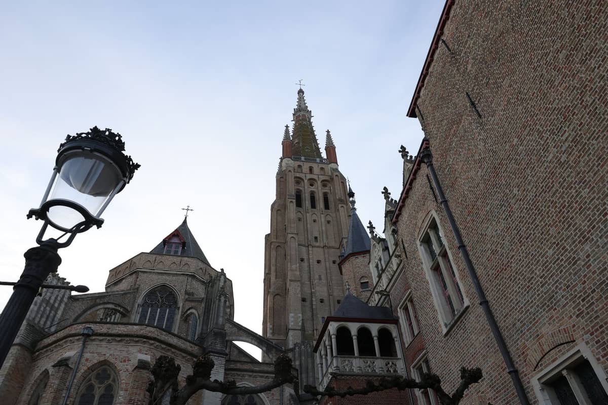 View up at the brick exterior and tower of the Church of Our Lady in Bruges under a blue sky.