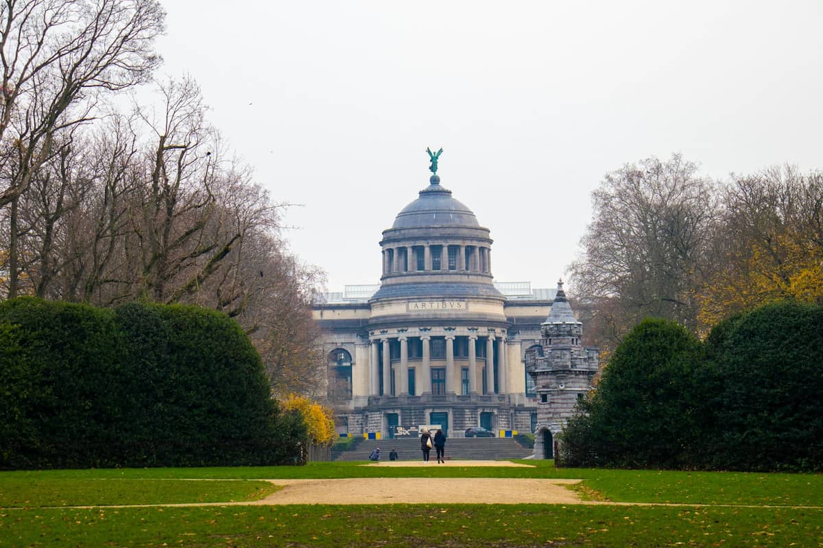 Fachada com cúpula de um importante edifício de museu no parque do Cinquantenaire de Bruxelas, vista entre árvores num dia nublado.