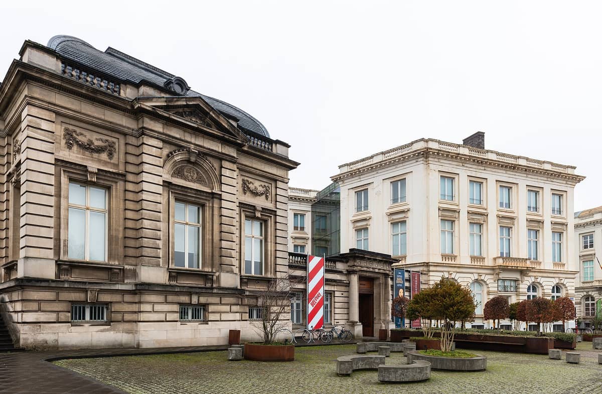 A fachada do Museu BELvue e do Palácio de Coudenberg em Bruxelas, com construções históricas e faixas do museu em um dia nublado.