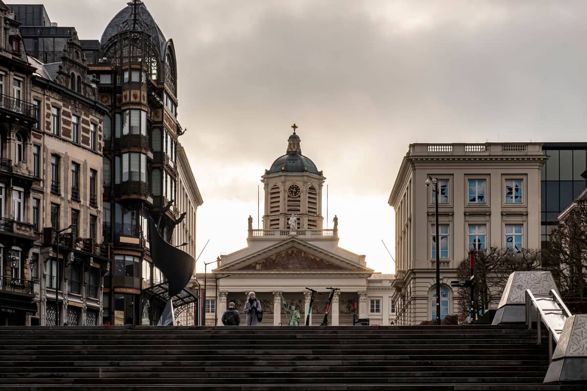 Vista da Place Royale em Bruxelas com o Museu Magritte, a igreja neoclássica e o edifício art nouveau Old England sob um céu dramático