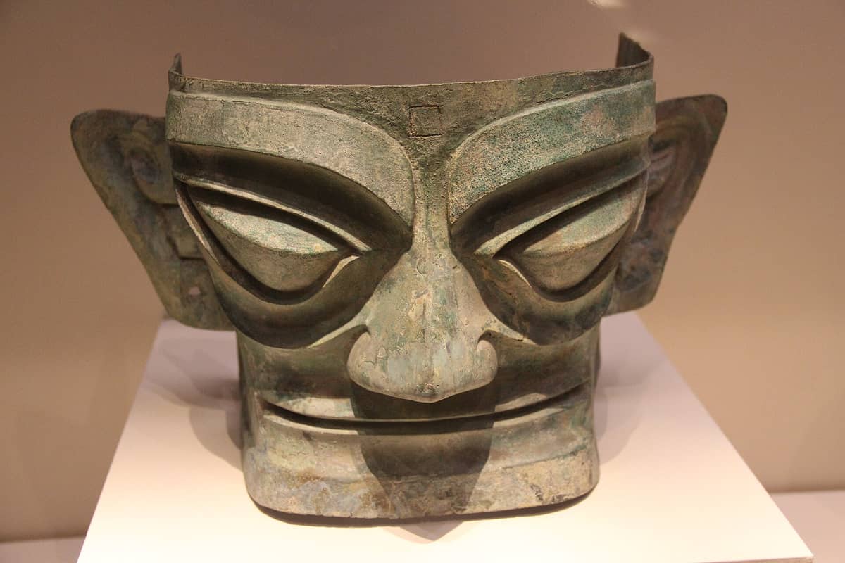 Eine detaillierte Bronzemaske mit großen Augen und Ohren aus der antiken Sanxingdui-Zivilisation, ausgestellt in einem Museum.