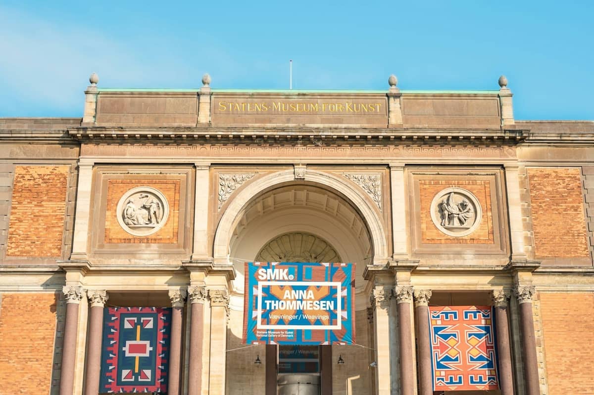 Główne wejście do Statens Museum for Kunst z banerami i klasycznymi detalami architektonicznymi pod błękitnym niebem
