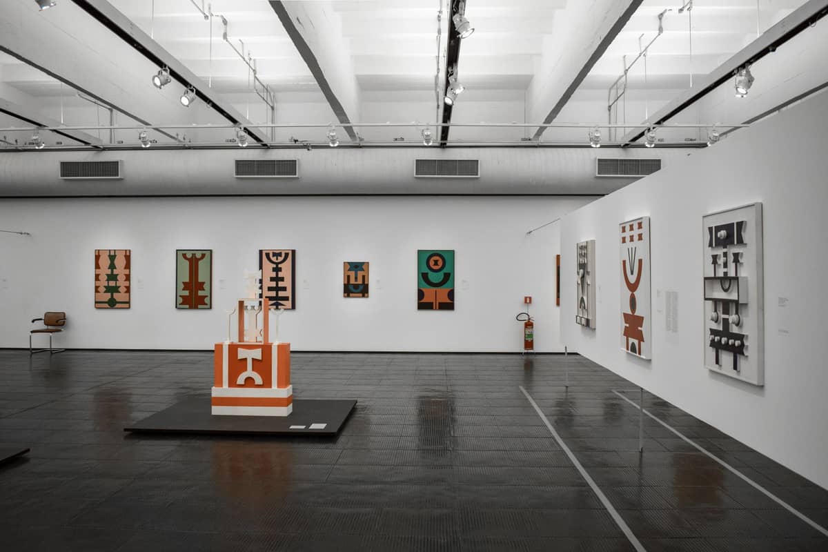Zeitgenössischer Kunstgalerieraum mit modernen abstrakten Gemälden und Skulpturen an weißen Wänden, heller Beleuchtung und einem geräumigen, klaren Interieur.