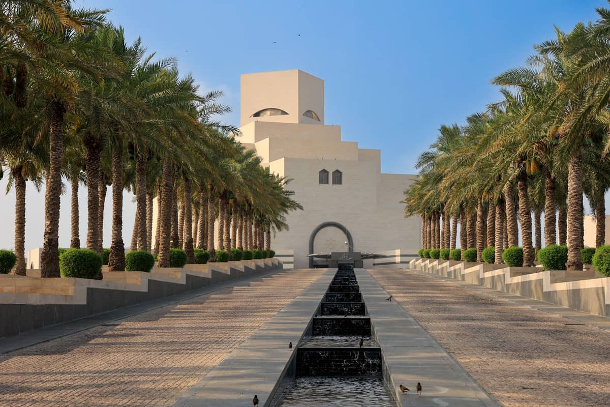 Das Museum für Islamische Kunst in Doha, Katar, vom palmengesäumten Eingang mit einem Wasserspiel im Zentrum unter einem klaren blauen Himmel.