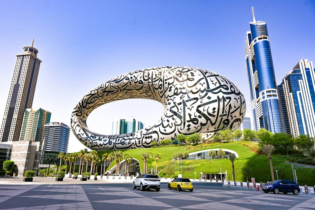 Das Museum of the Future in Dubai – ein markantes, torusförmiges Silbergebäude mit arabischer Kalligrafie, umgeben von Wolkenkratzern und grüner Bepflanzung an einem hellen Tag.