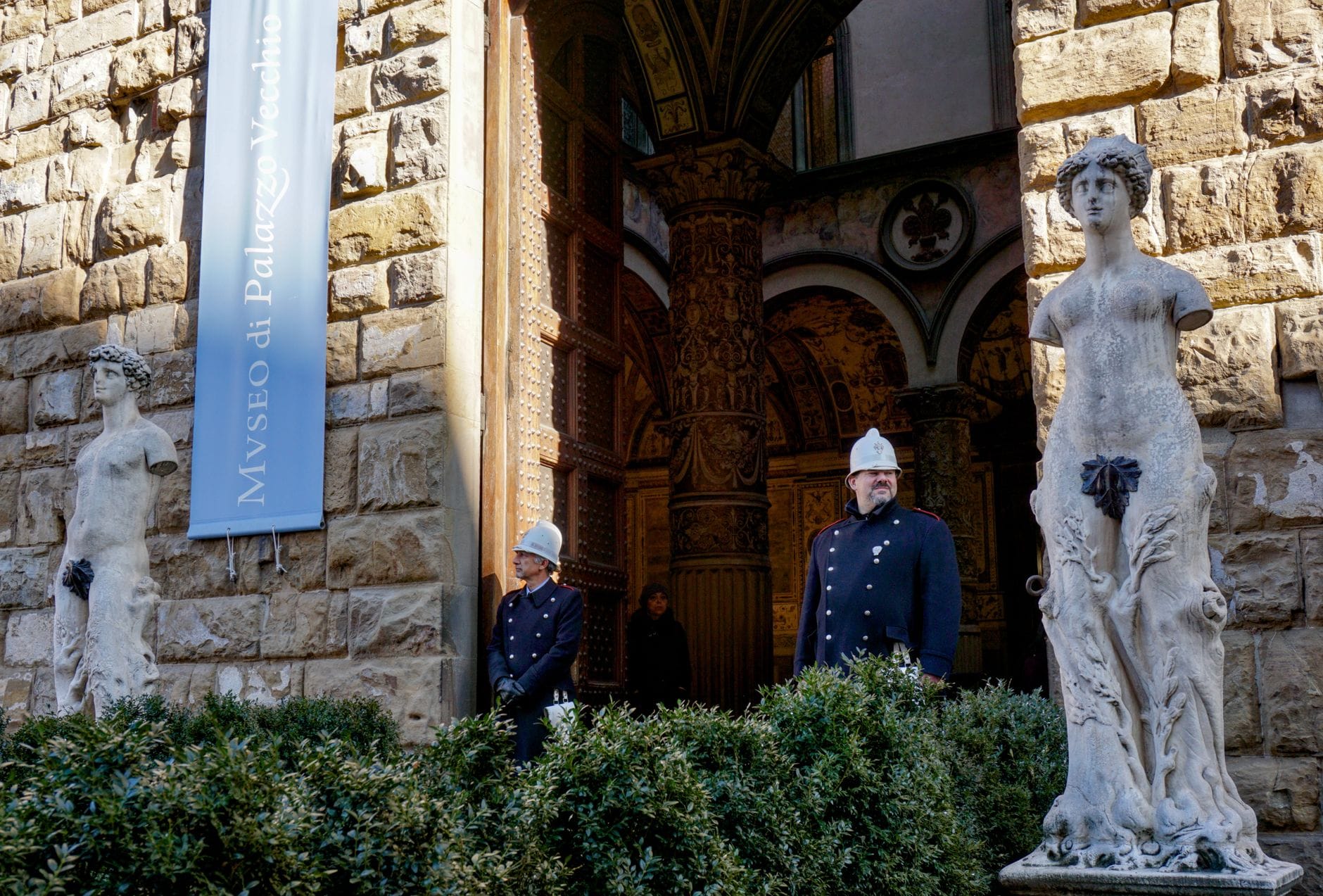 ทางเข้า Museo di Palazzo Vecchio ในเมืองฟลอเรนซ์ พร้อมงานหินแกะสลักอันวิจิตร รูปปั้น และเจ้าหน้าที่รักษาความปลอดภัยสวมเครื่องแบบยืนอยู่หน้าประตู
