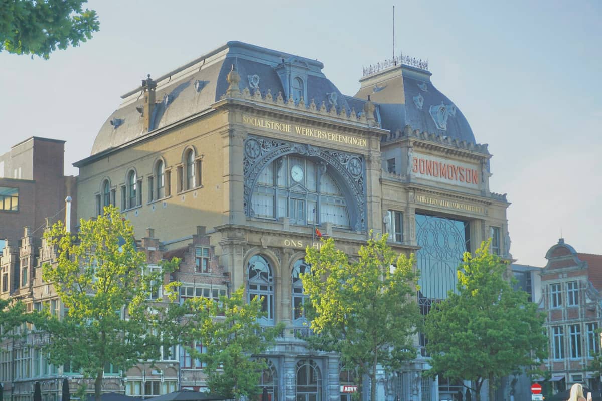 Art Nouveau façade of the Design Museum Gent building with ornate windows and trees in front, under a clear blue sky.