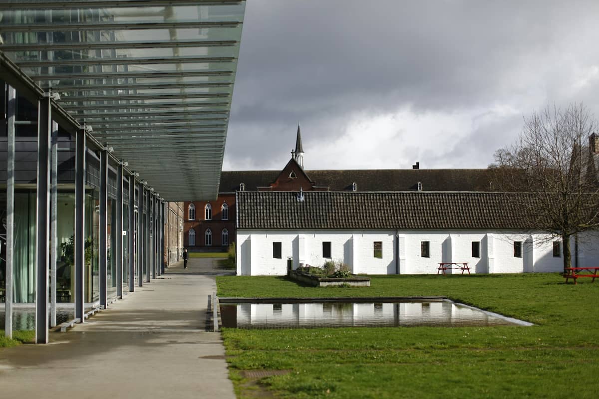Exterior view of the STAM Ghent City Museum with its glass entrance, white buildings, and a shallow reflecting pool in front.