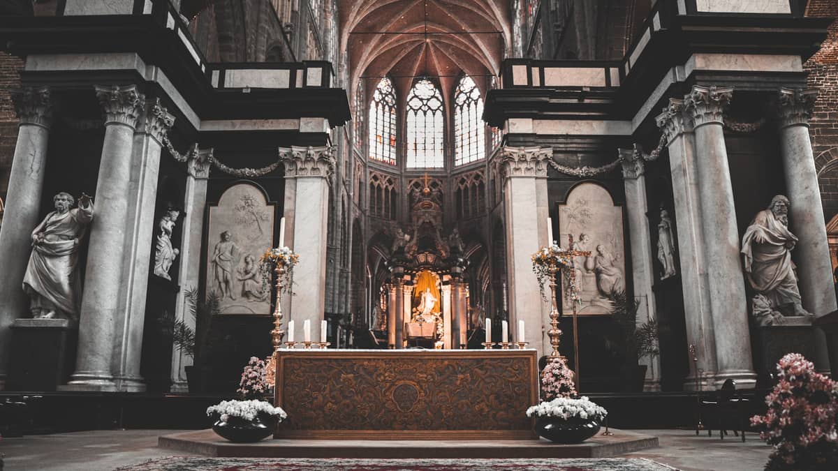 The ornate altar of an old European church with classical columns, marble statues, and vaulted ceilings, evoking fine art in Ghent.
