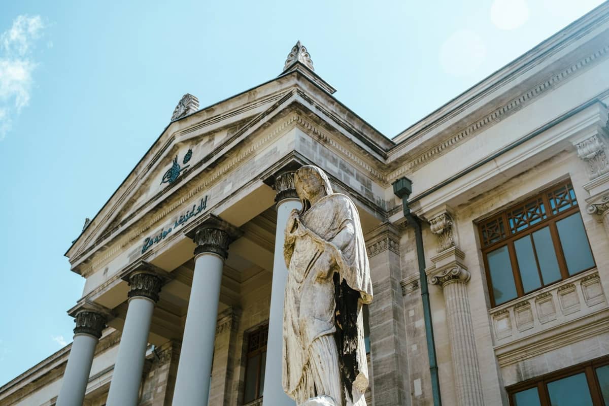Vista de cerca de la entrada de los Museos Arqueológicos de Estambul con columnas y una estatua antigua bajo un cielo azul.