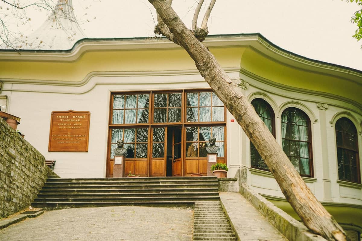 Fachada de un museo único en Estambul con una placa, escalones, ventanas arqueadas y un árbol inclinado al frente.