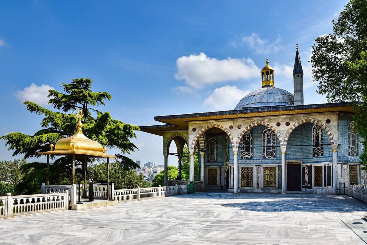 Una impresionante vista del Palacio de Topkapı en Estambul bajo un cielo azul brillante, mostrando su ornamentado pabellón con cúpula y su elegante terraza de mármol.