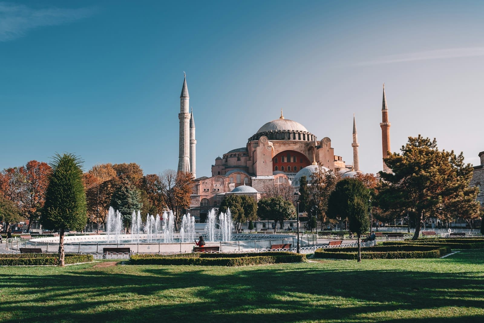 Vista ampla e vibrante de Hagia Sophia com minaretes, parque verde exuberante, árvores e uma fonte central em um dia ensolarado em Istambul.