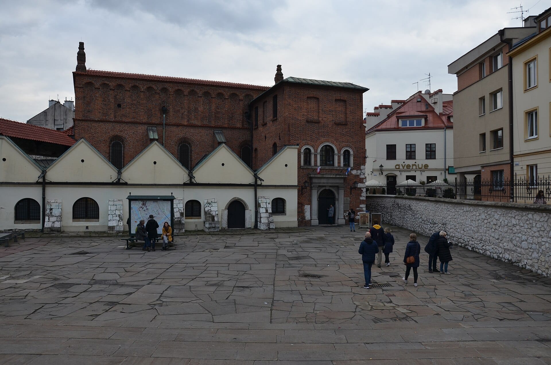 ด้านนอกของ Old Synagogue แห่งเมือง Kraków ซึ่งเป็นพิพิธภัณฑ์มรดกชาวยิวที่สำคัญ พร้อมผู้คนเดินอยู่บริเวณลานด้านหน้าใน Kazimierz