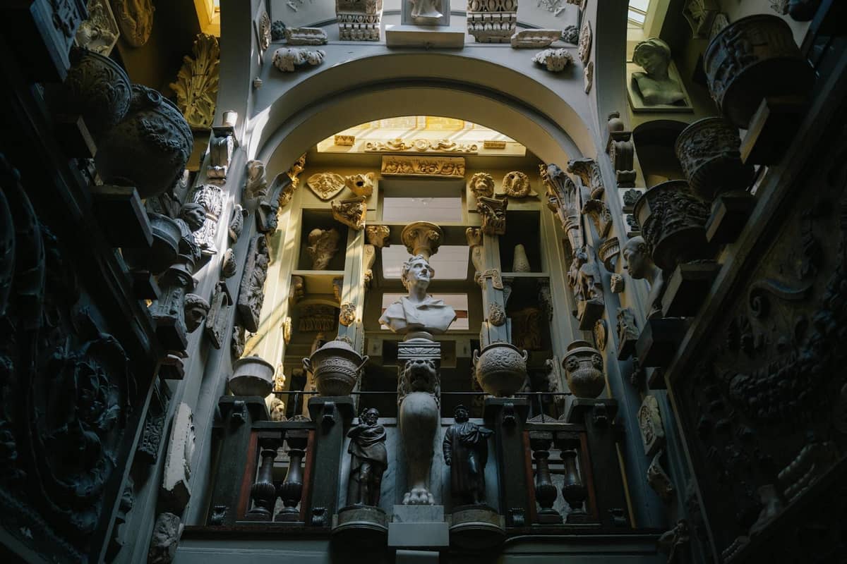 Interior eclético de museu repleto de esculturas, bustos e ornamentos clássicos, dispostos densamente em paredes com prateleiras sob uma claraboia arqueada.