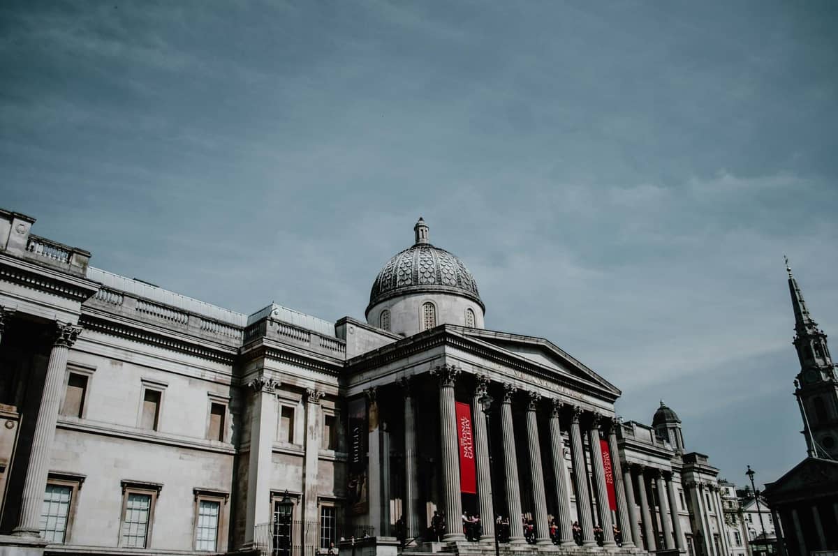 A grandiosa fachada neoclássica da National Gallery em Londres com altas colunas e cúpula, sob um céu limpo.