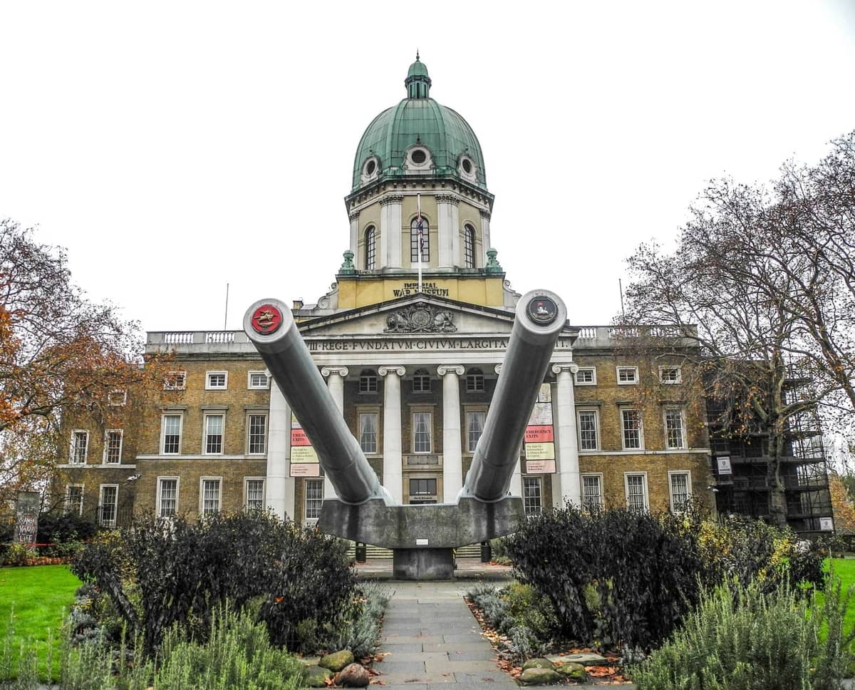 Imponente entrada de museu em Londres com uma cúpula e dois canhões navais gémeos, com uma fachada histórica clássica rodeada de jardins.