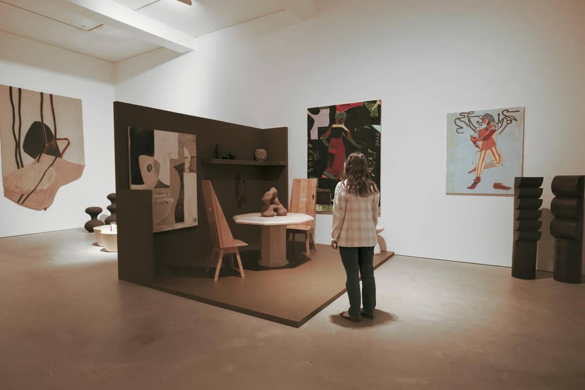 Pessoa apreciando instalações de arte contemporânea e pinturas modernas em um espaço de galeria limpo e bem iluminado.
