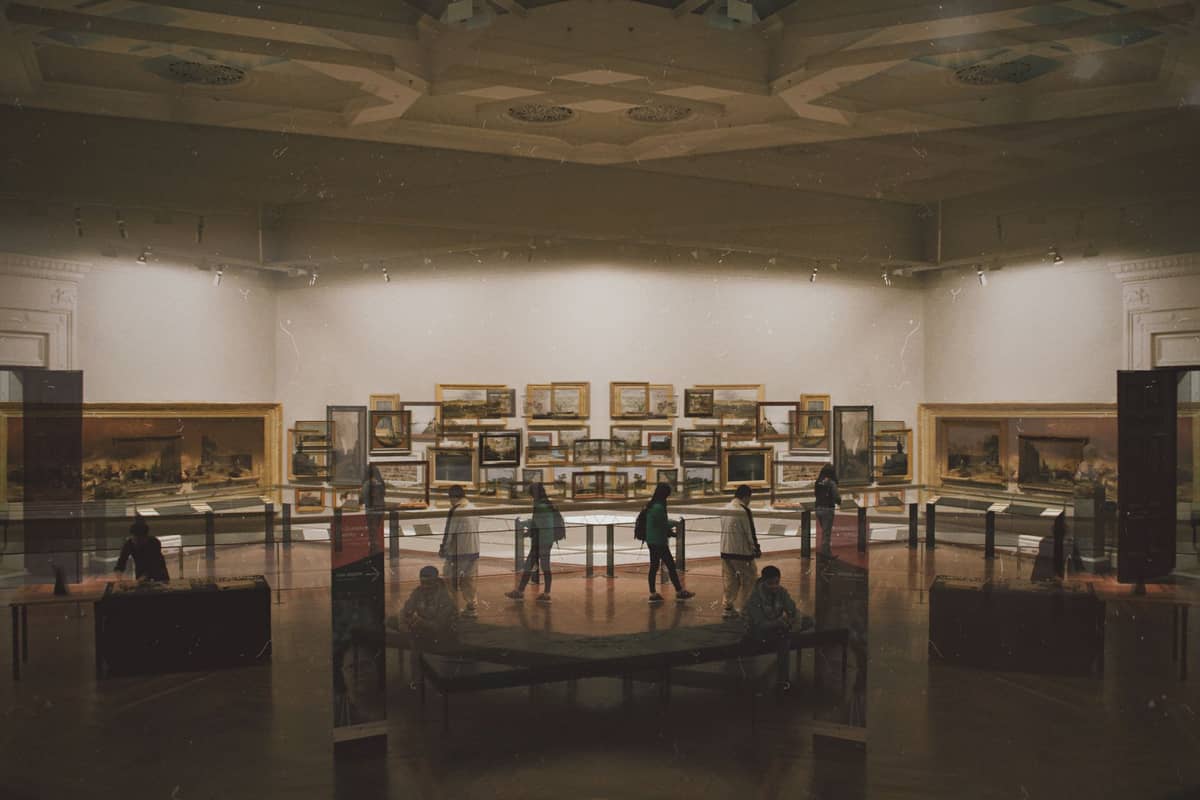 Interior con poca luz de una galería de arte en un museo de Melbourne, con visitantes observando pinturas y exhibiciones.