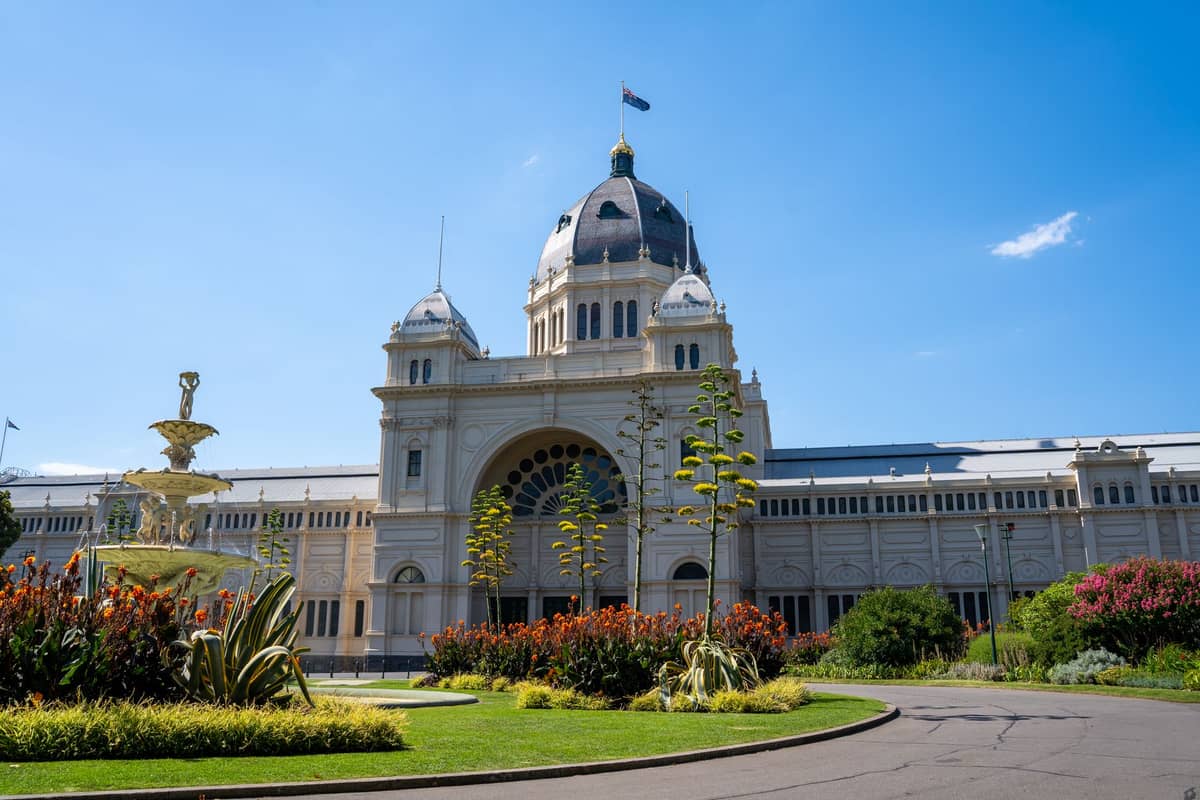 Royal Exhibition Building em Melbourne com seu teto abobadado, jardins exuberantes, uma fonte de água e céu azul claro.