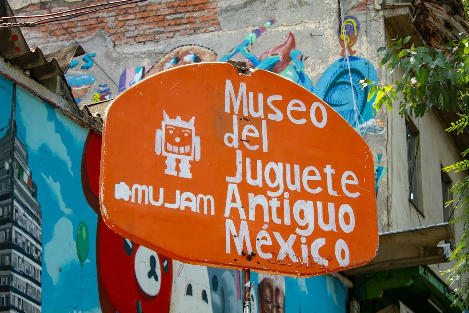 Placa do Museo del Juguete Antiguo México, rodeada por coloridos murais urbanos.
