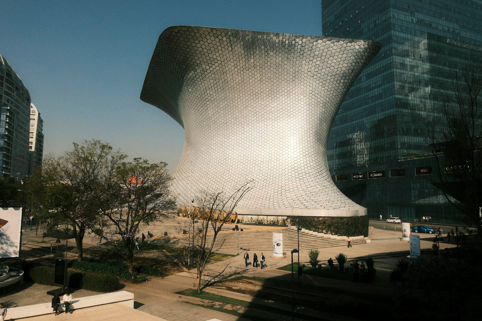 Impressionante edifício de museu com azulejos hexagonais prateados e curvas dramáticas em uma praça urbana moderna, com pessoas caminhando nas proximidades em Polanco, Cidade do México.