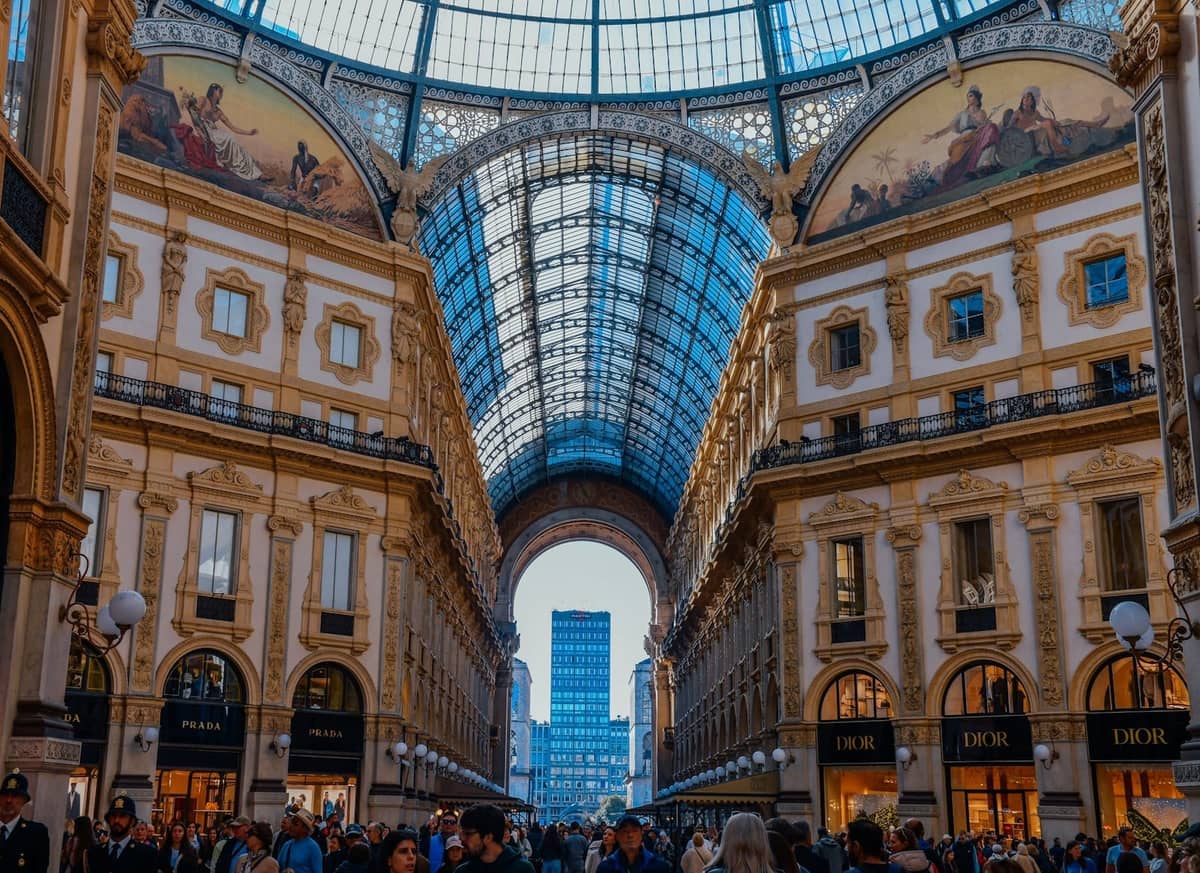 Die elegante Galleria Vittorio Emanuele II in Mailand mit Glasdach, Menschenmassen vor Designergeschäften und prächtiger Architektur.