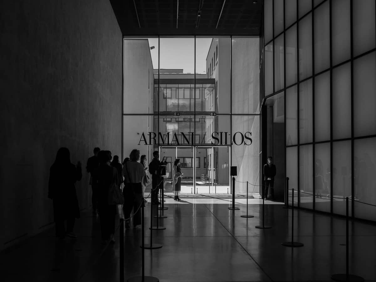 Modernes Glaseingangsfoyer des Armani Silos Museums in Mailand mit stehenden und gehenden Personen im Inneren.